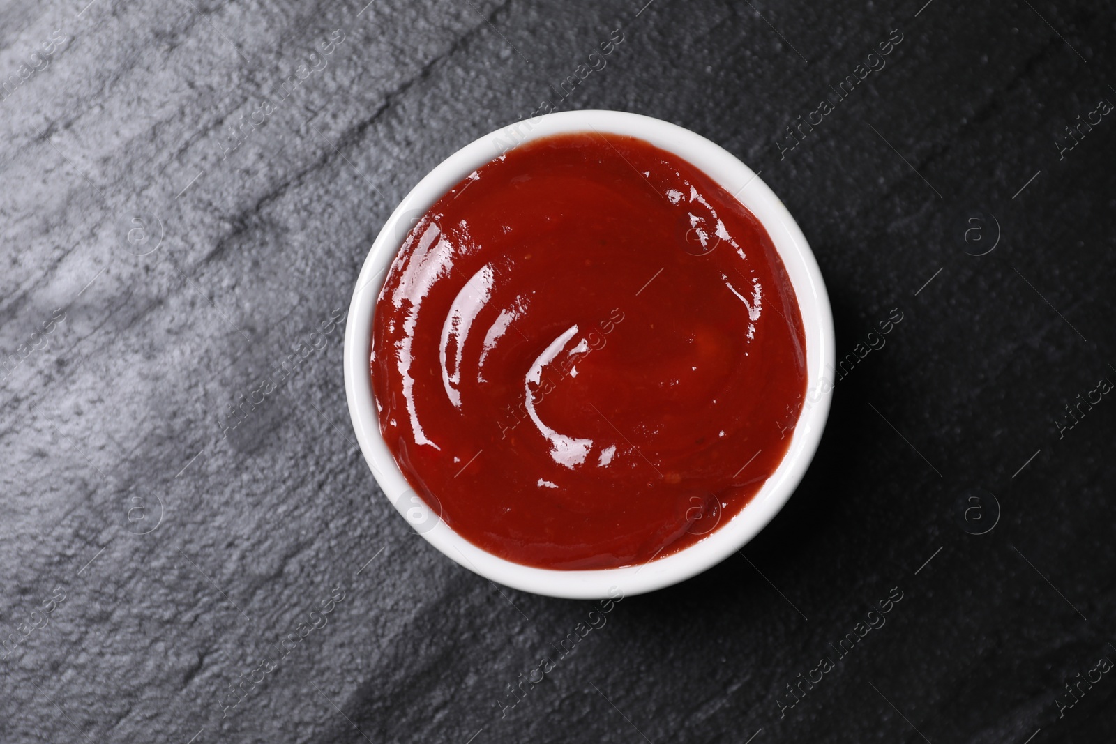 Photo of Organic ketchup in bowl on black table, top view. Tomato sauce