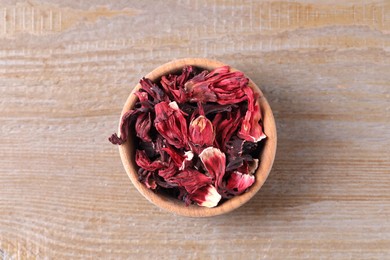 Dry hibiscus tea in bowl on wooden table, top view