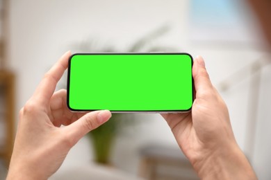 Image of Woman holding smartphone with green screen indoors, closeup. Gadget display with chroma key. Mockup for design