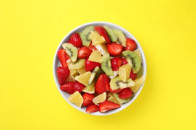 Yummy fruit salad in bowl on yellow background, top view