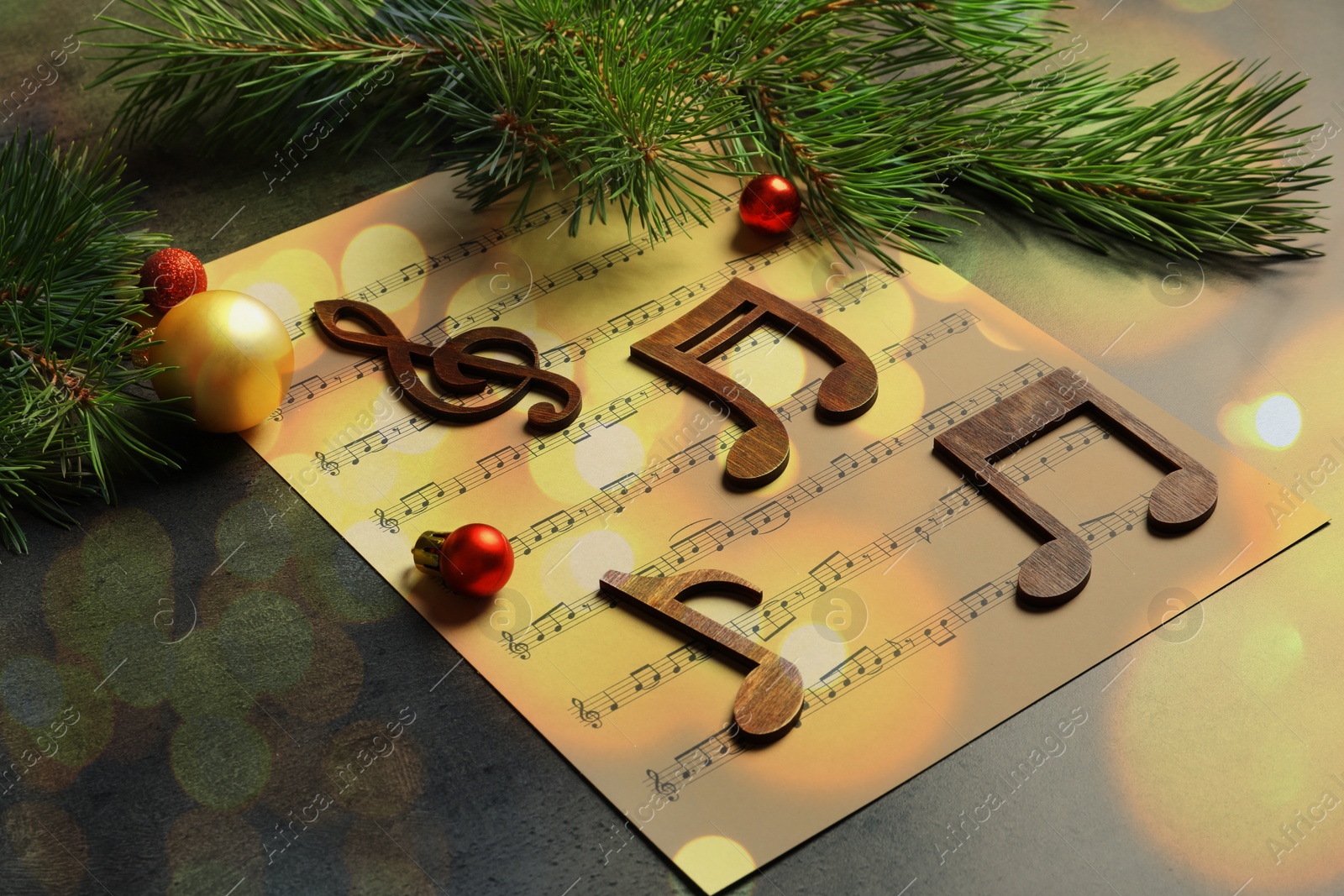 Image of Christmas and New Year music. Fir tree branch, festive balls, music sheet and wooden notes on table, bokeh effect