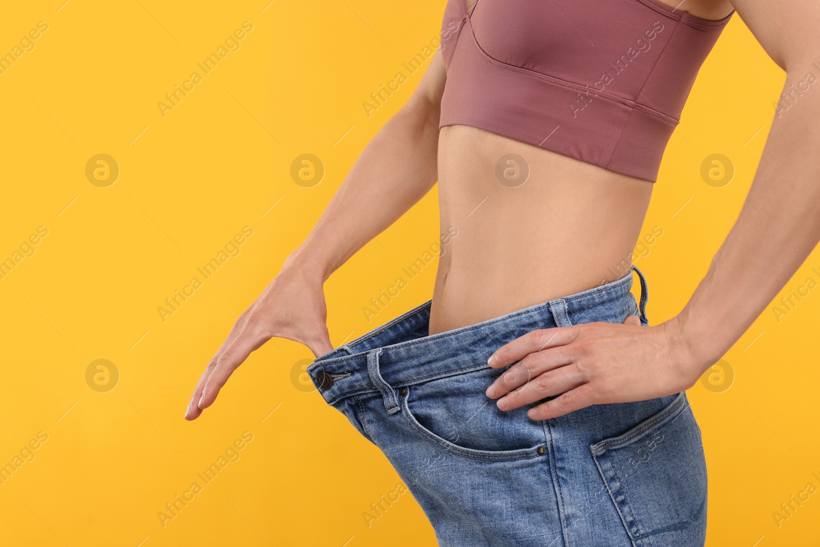 Photo of Slim woman wearing big jeans on yellow background, closeup. Weight loss