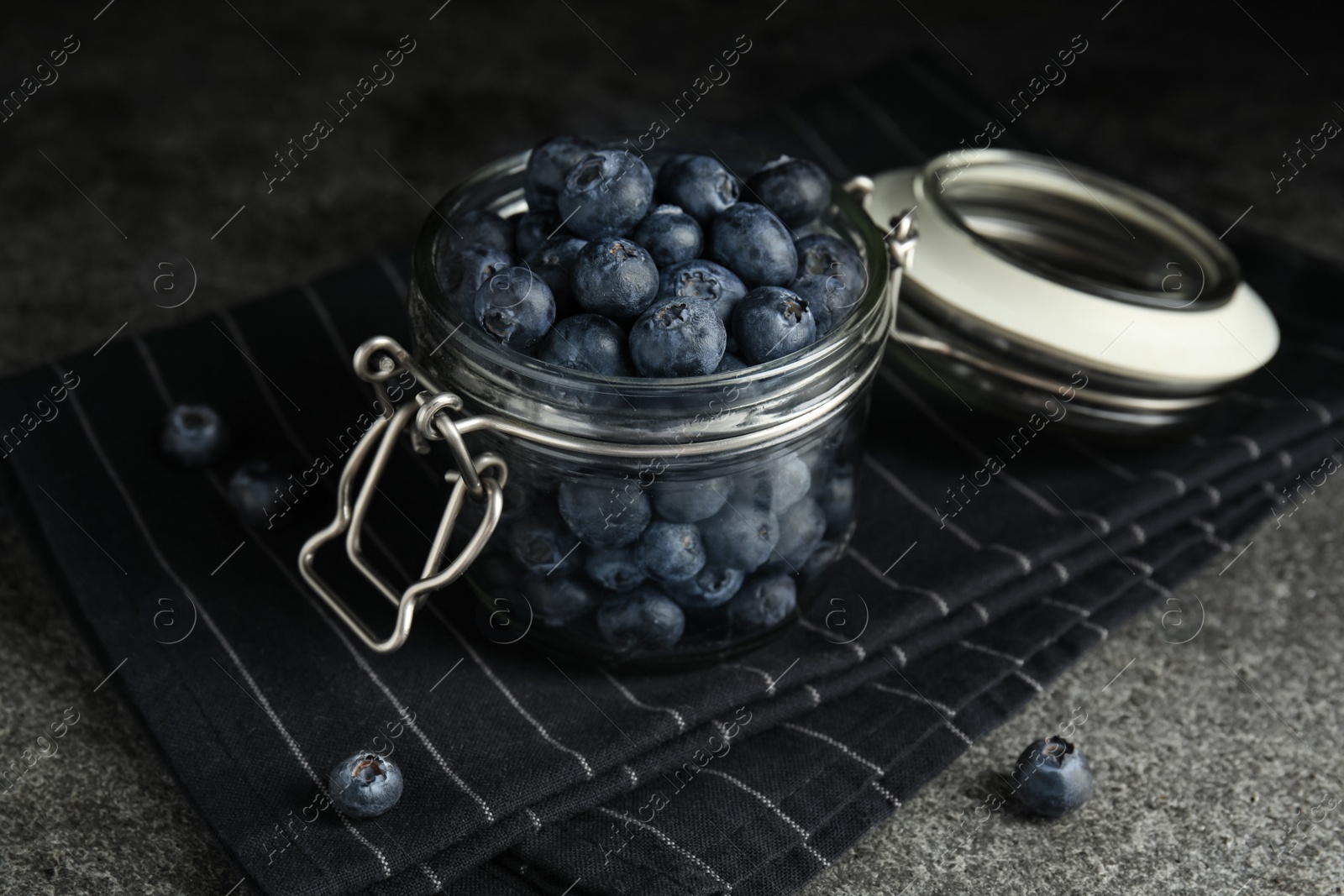 Photo of Tasty ripe blueberries in glass jar on grey table