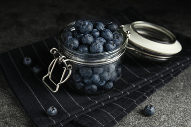 Tasty ripe blueberries in glass jar on grey table