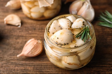 Photo of Preserved garlic in glass jar on wooden table, closeup