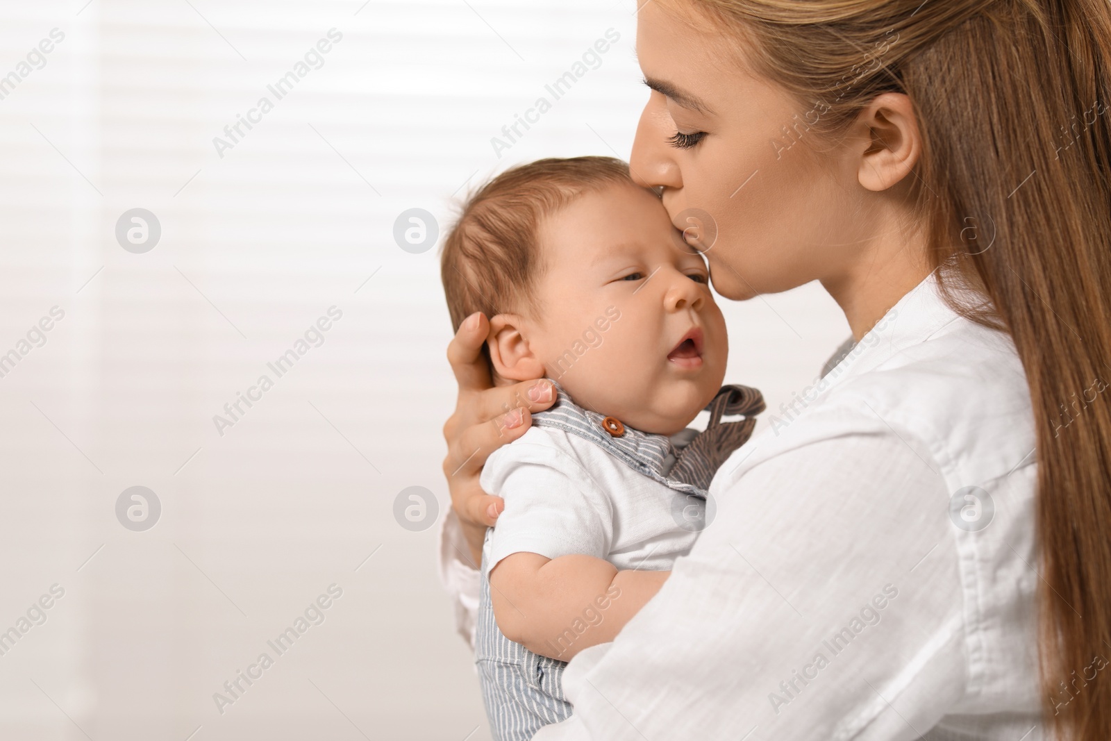 Photo of Mother kissing her cute newborn baby indoors, space for text