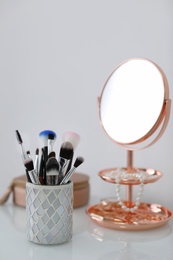 Makeup brushes in holder on table against light background