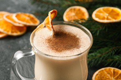 Photo of Glass cup of delicious eggnog with dried orange slice and cinnamon on gray table, closeup