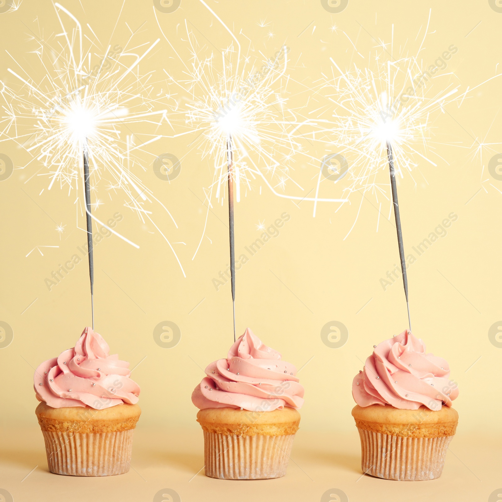 Image of Birthday cupcakes with sparklers on light yellow background