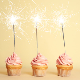 Birthday cupcakes with sparklers on light yellow background