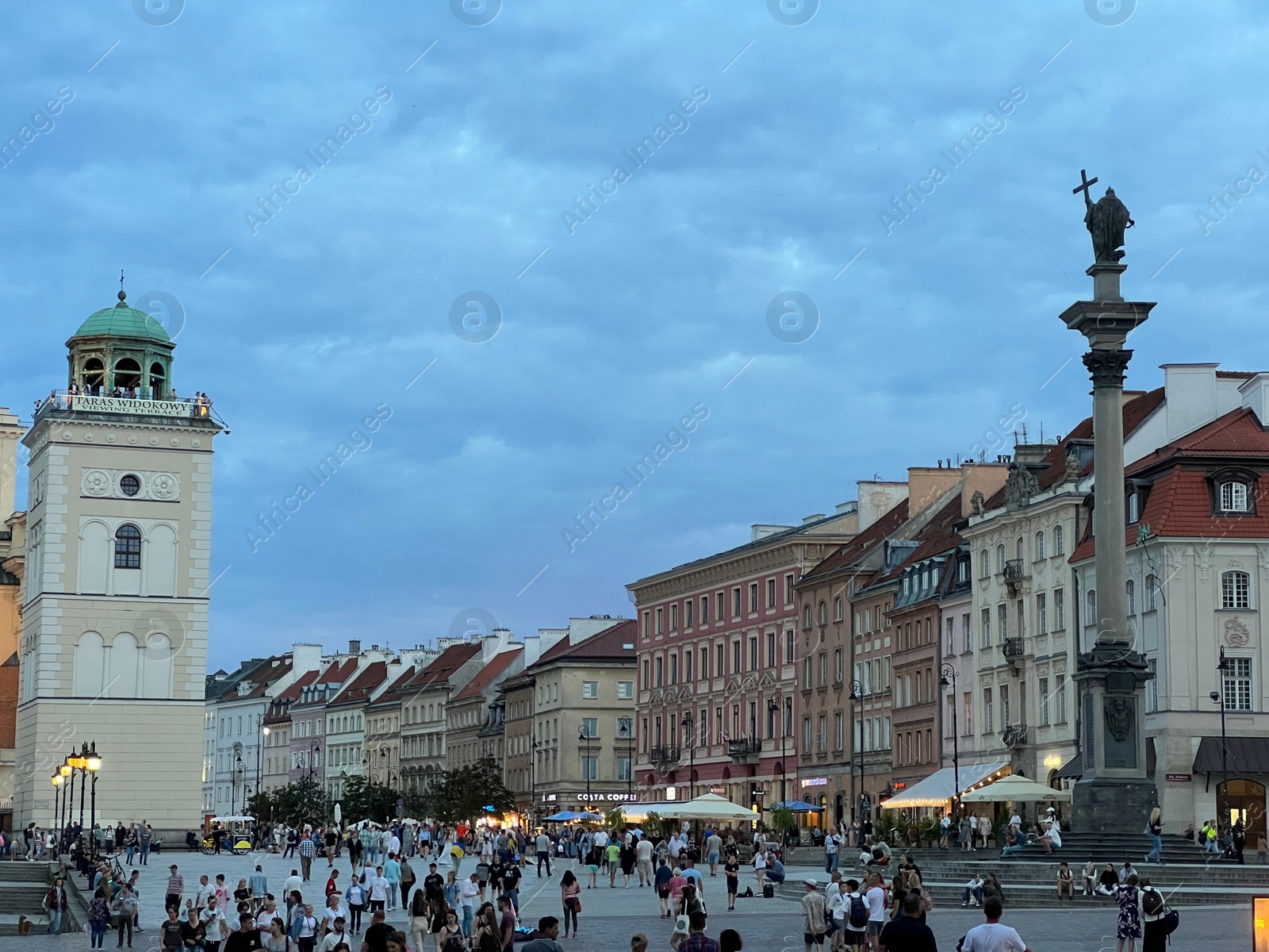 Photo of WARSAW, POLAND - JULY 15, 2022: View of crowded Old Town Market Place under cloudy sky in evening