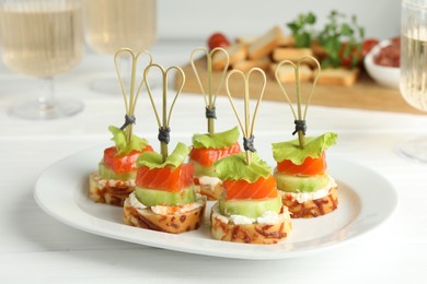 Tasty canapes with salmon, cucumber, bread and cream cheese on white wooden table, closeup