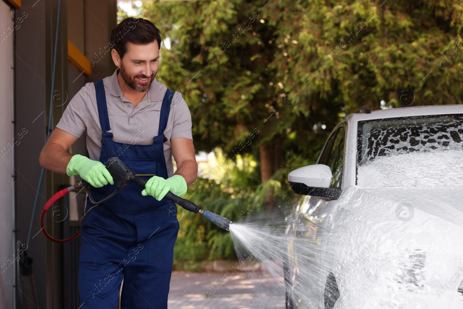 Photo of Worker washing auto with high pressure water jet at outdoor car wash