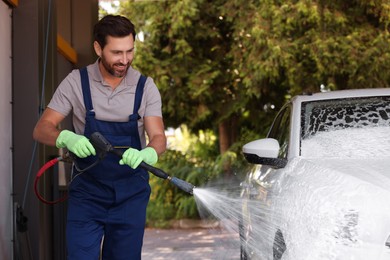 Photo of Worker washing auto with high pressure water jet at outdoor car wash