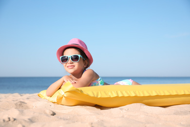 Cute little child with inflatable mattress lying at sandy beach on sunny day