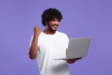 Happy man with laptop on purple background, space for text