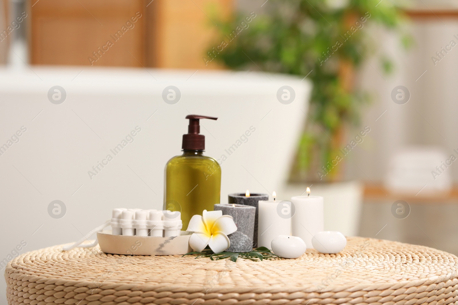 Photo of Spa products, burning candles and plumeria flower on wicker table in bathroom