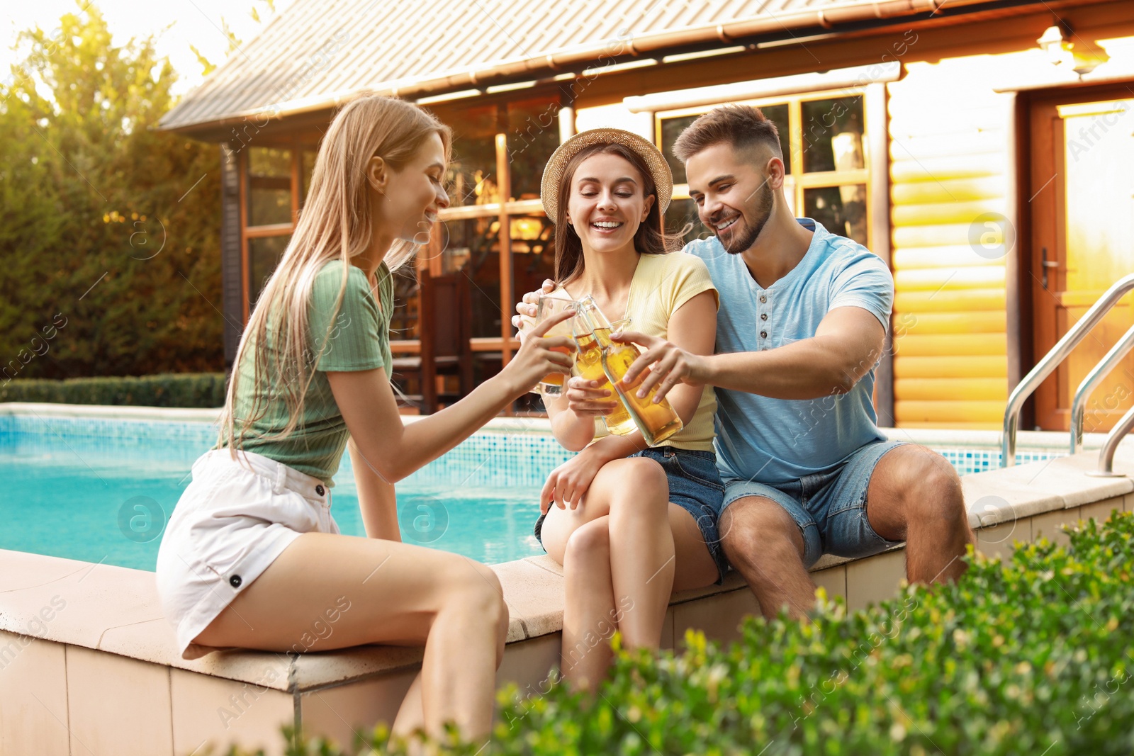 Photo of Happy friends with drinks at barbecue party near swimming pool outdoors