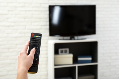 Photo of Woman changing TV channel with remote control in living room, focus on hand. Space for text