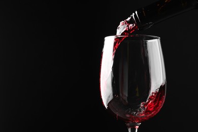 Photo of Pouring red wine into glass against black background, closeup. Space for text