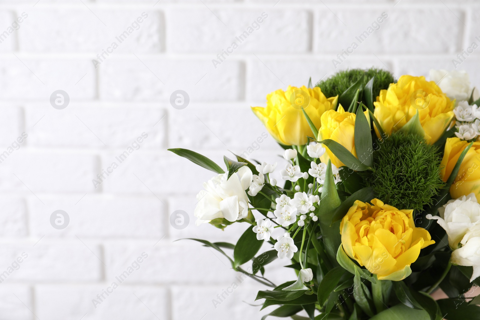 Photo of Beautiful bouquet with peony tulips near white brick wall, closeup. Space for text