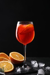 Photo of Glass of tasty Aperol spritz cocktail with orange slices and ice cubes on table against black background
