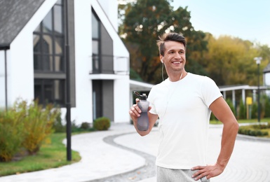 Young man with earphones drinking water after running on street. Healthy lifestyle