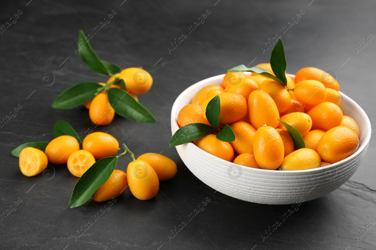 Photo of Fresh ripe kumquats in bowl on black table
