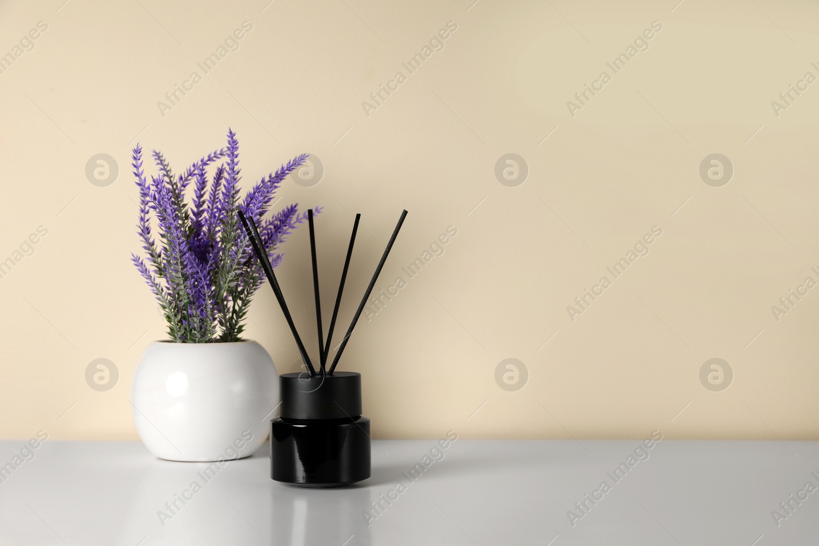 Photo of Aromatic reed air freshener and lavender flowers on white table indoors. Space for text