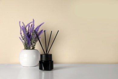 Photo of Aromatic reed air freshener and lavender flowers on white table indoors. Space for text