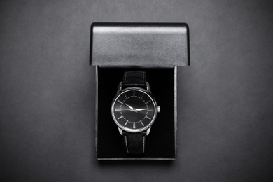 Elegant wristwatch in box on black background, top view