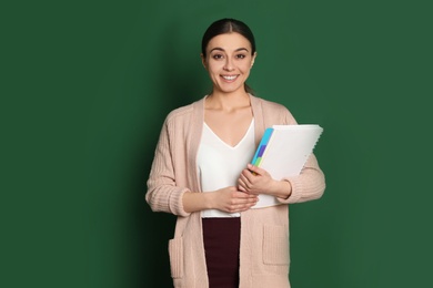 Portrait of young teacher with notebook on green background