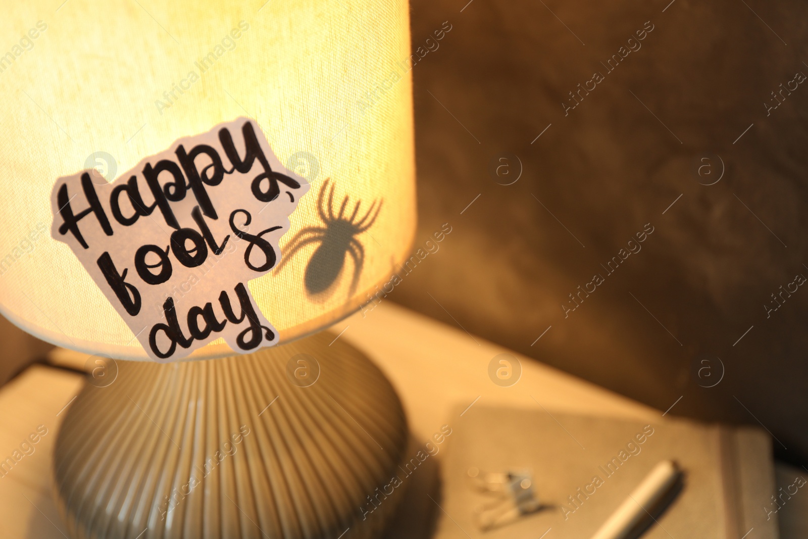 Photo of Glowing lamp with spider and words Happy Fool's Day on nightstand. Space for text