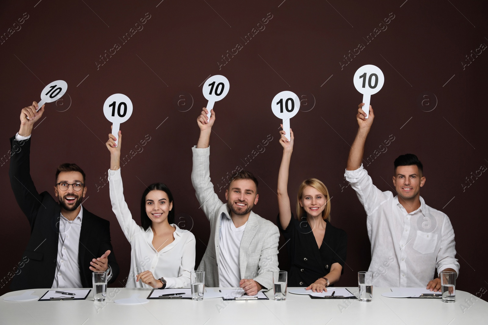 Photo of Panel of judges holding signs with highest score at table on brown background