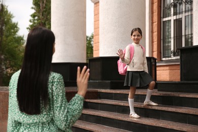 Little girl waving goodbye to mother near school entrance outdoors