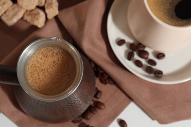 Photo of Turkish coffee. Cezve and cup with hot aromatic coffee, beans and sugar on table, flat lay