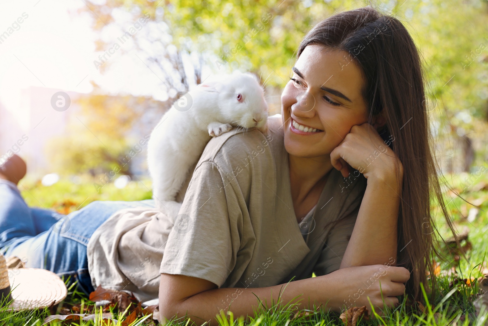 Photo of Happy woman with cute white rabbit on grass in park