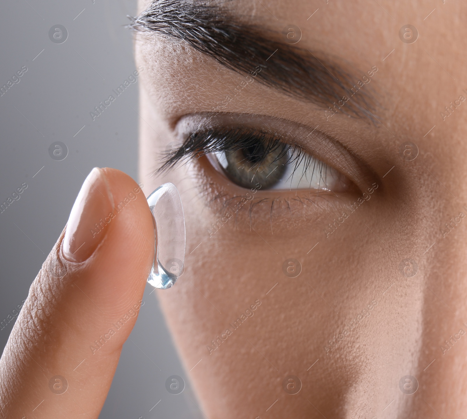 Photo of Young woman putting contact lens in her eye, closeup