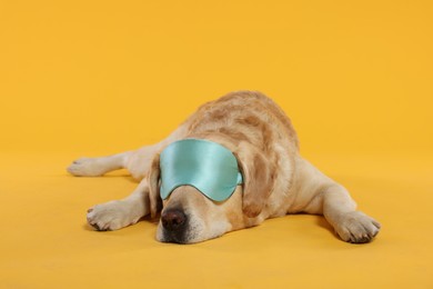 Photo of Cute Labrador Retriever with sleep mask resting on yellow background
