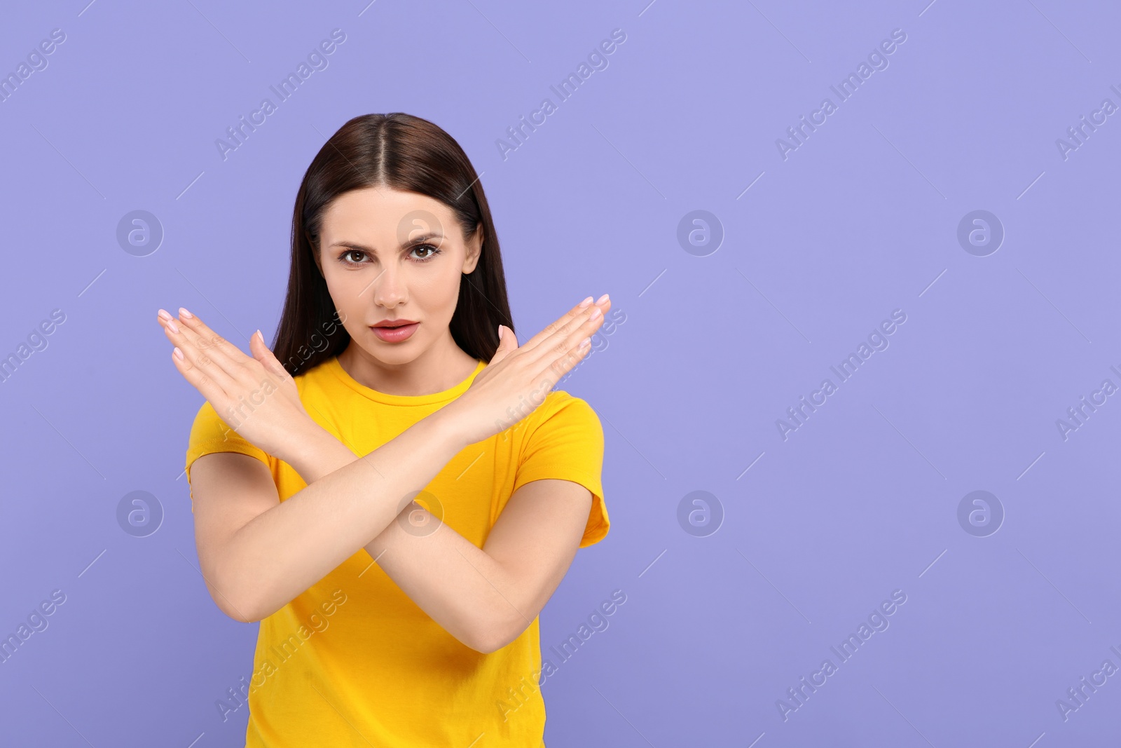 Photo of Stop gesture. Woman with crossed hands on violet background, space for text