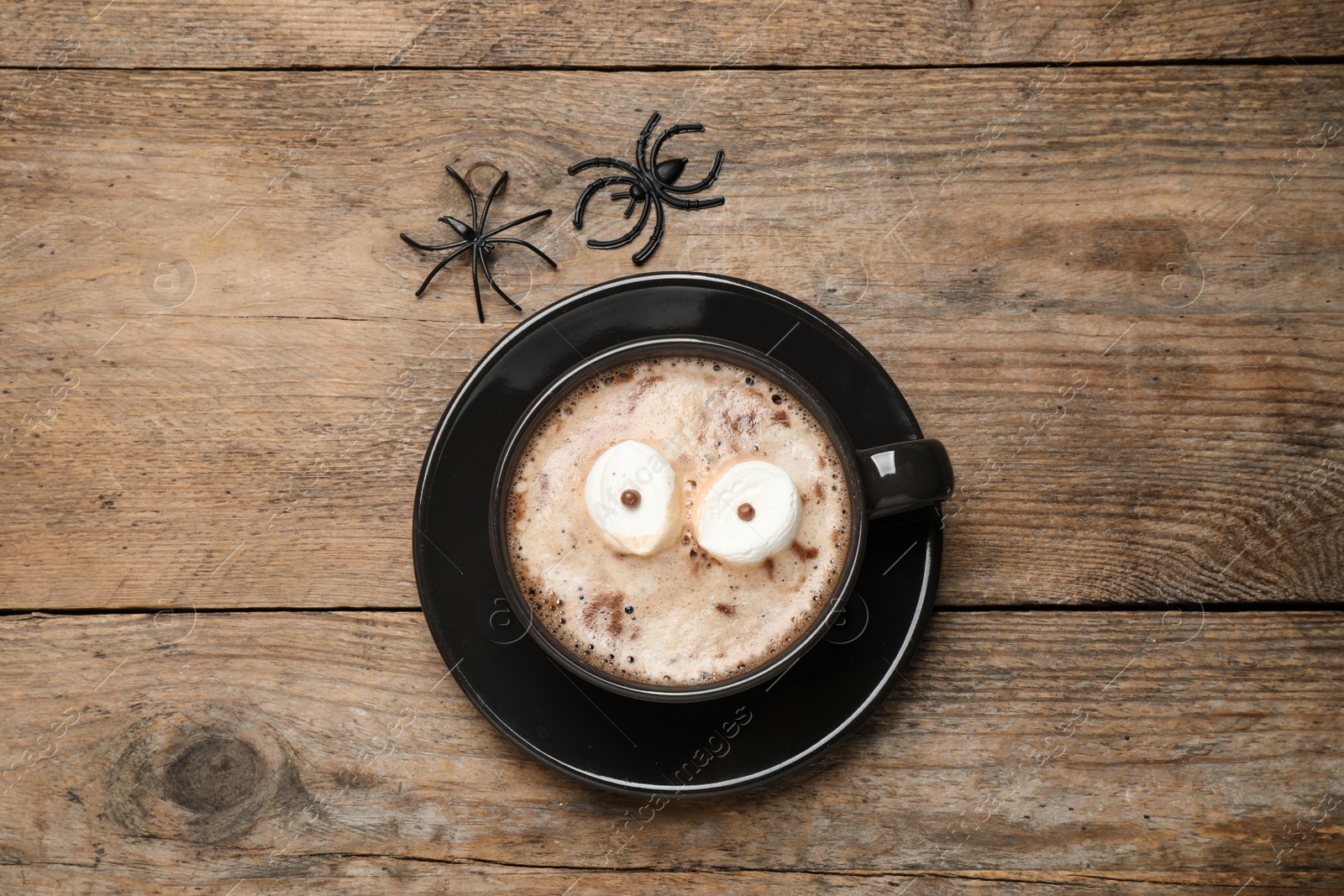 Photo of Cup of coffee decorated with marshmallow eyes on wooden table, flat lay. Halloween celebration