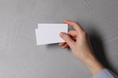 Photo of Woman holding blank cards at light grey table, top view. Mockup for design