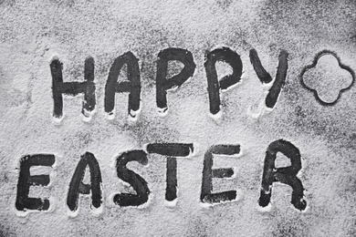 Words Happy Easter written in flour on black table, top view. Baking cake