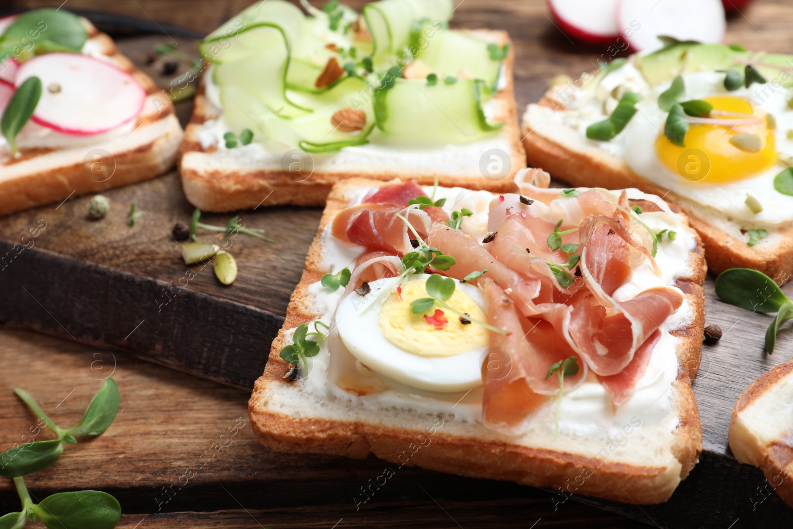 Photo of Different delicious sandwiches with microgreens on wooden board, closeup