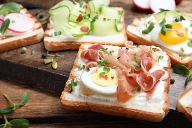 Different delicious sandwiches with microgreens on wooden board, closeup