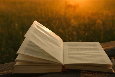 Photo of Open book on wooden bench in field at sunset, closeup