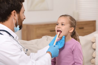 Doctor examining girl`s oral cavity with tongue depressor indoors
