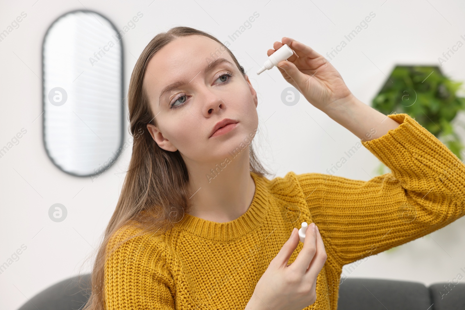 Photo of Young woman applying medical ear drops indoors