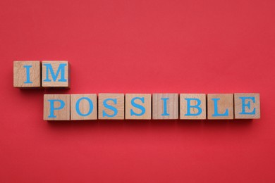 Photo of Motivation concept. Changing word from Impossible into Possible by removing wooden cubes on red background, flat lay