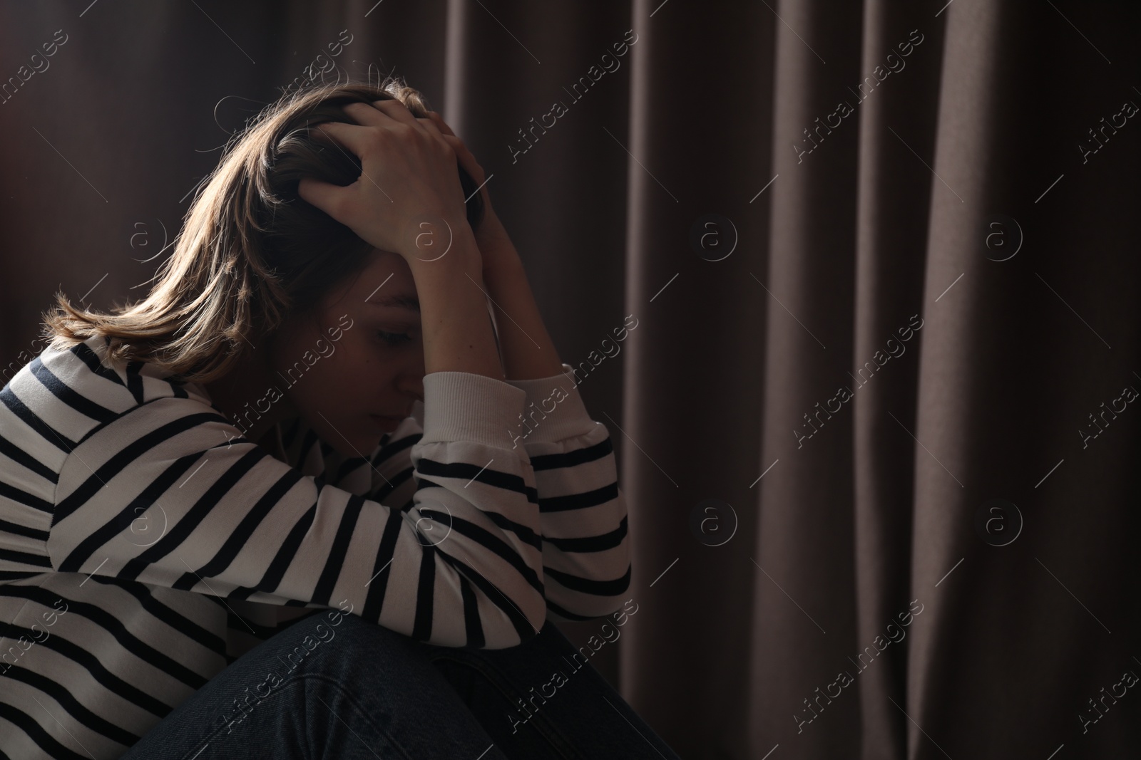 Photo of Sad young woman near curtains indoors, space for text